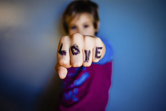 Close-up of girl showing fingers with love text while standing by wall at home