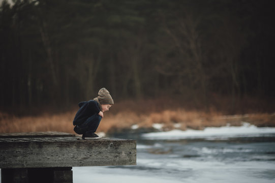 Side view of curious boy looking at river while crouching on wood at park