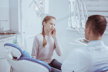 Teeth issue. Top view of appealing girl touching face while staring at male dentist