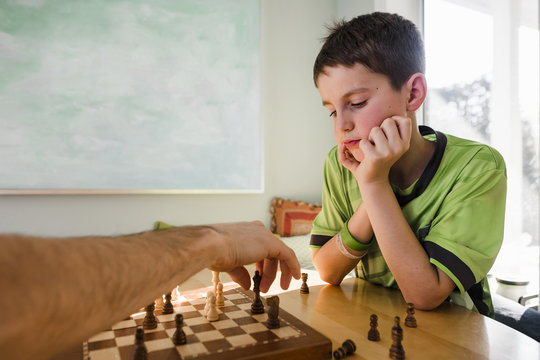 Cropped hand of father playing chess with son on table at home