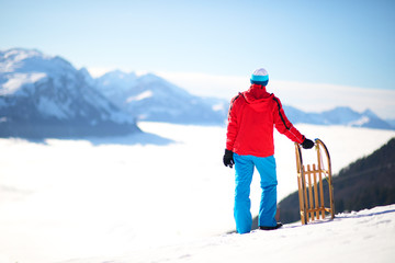 Young attractive man ready to go sledding in Swiss Alps during winter holiday.