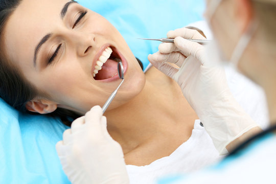 Young female patient visiting dentist office.Beautiful woman with healthy straight white teeth sitting at dental chair with open mouth during oral checkup while doctor working at teeth