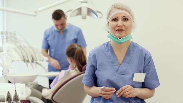 Professional woman dentist talking in office on background with dental assistant working 