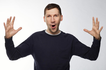 Happy surprised young American male wearing dark blue jacket  gesturing with hands as if showing size of something big, looking at camera in shock, keeping mouth wide open. Human emotions, expressions