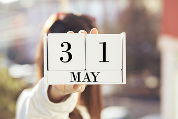 the woman is holding a white wooden calendar. White  wooden cube shape calendar for MAY 31 with hand 