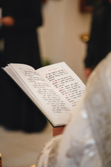 Naklejka premium Christening in the church, priest is reading a prayer from the Bible. Details in the orthodox christian church