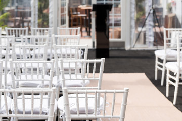 White wedding chairs for ceremony with background of rows of many seats pattern, aisle and podium in venue, restaurant, building outdoors