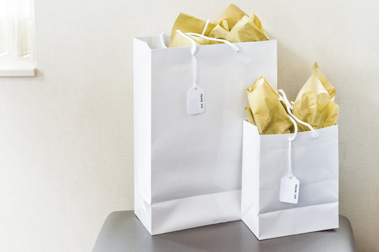 Two Large Gift Bags With Thank You Note Text Tags On Chair Table In Room Isolated, Golden Yellow Wrapping Paper By Window Wall Closeup