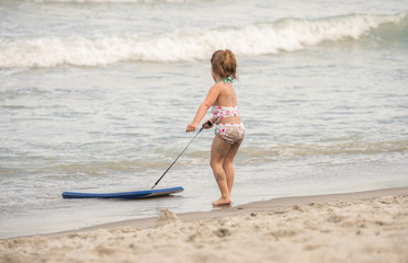 unknown little girl pulls her board to shore