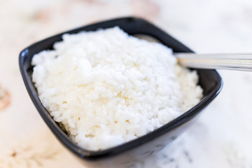 Macro closeup of plain white boiled short or medium grain rice in black bowl, serving spoon on table showing detail and texture