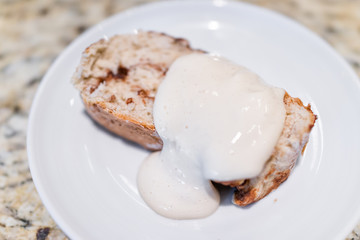Macro closeup of homemade healthy vegan golden baked whole cinnamon roll cake slice bread on plate with tofu icing cream on table