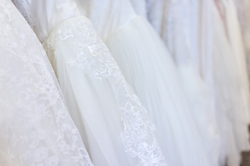 Fototapeta na wymiar Many wedding dresses in boutique discount store, white garments hanging on rack hangers row closeup with white lace, tulle, design