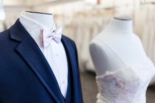 Closeup of bride and groom mannequin in blue, pink wedding attire suit, butterfly necktie, tie and white gown in boutique store, shop