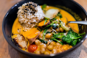 Closeup of Indian meal lunch or dinner dish in traditional Asian restaurant or cafe with vegetable sweet potato orange curry, sesame seeds, brown rice, green cilantro parsley garnish, chickpeas