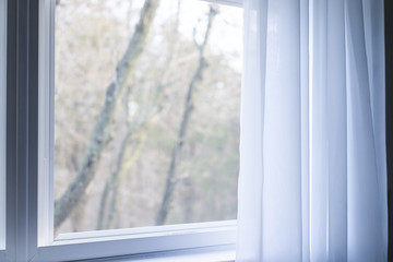 Closeup of plain white window curtains blinds in blue room interior indoors with wind decoration, outside bare tree branches in winter
