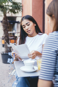 Woman reading documents while sitting with friend by table at sidewalk cafe