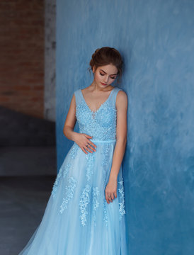 Young blonde girl in a luxurious blue dress with tulle and lace. Delicate natural make-up. Beautiful, elegant, high hairstyle for an average length of hair, with weaving. Evening image