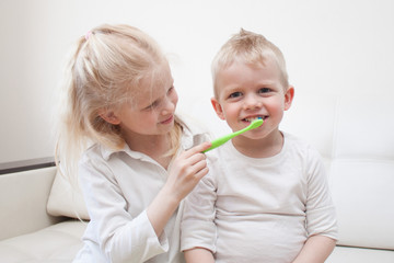 Little cute blonde girl is brushing the boy's teeth. Fun lifestile play dentist game. Children smile. Health care, dental hygiene