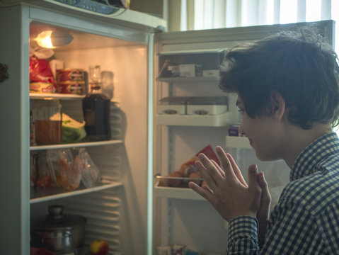 Young Hungry Teenager Looking For Food In The Opened Fridge