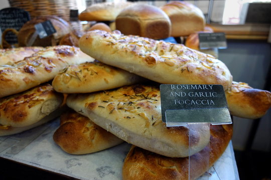 Shallow focus close up of rosemary and garlic focaccia bread, with other loaves in blurred background