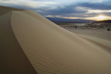 Fototapeta na wymiar Sand dunes curve under a cloudy sky to create a dramatic landscape.