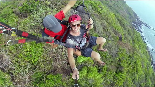 Two men flying on paraplane above cliff break and sea shore gopro selfie