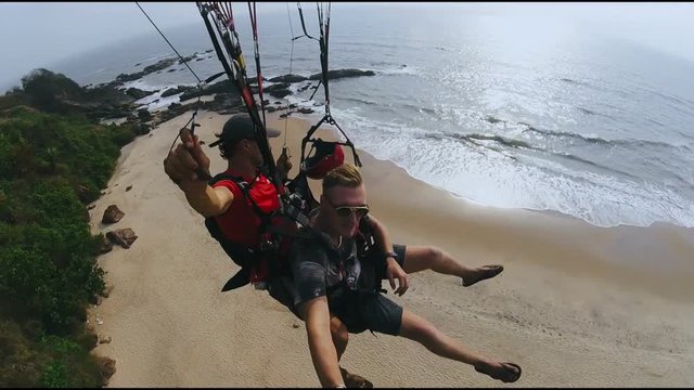 Two men flying on paraplane above rocky mountain and taking off on ocean beach