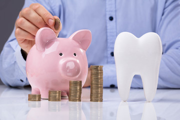 White Tooth Beside Man Inserting Coin In Piggy Bank