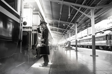 Asian man standing and looking at train wearing a black suit,  black and white photography