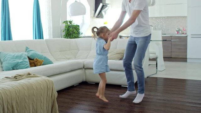 Medium shot of cute little girl and happy father holding hands and jumping while playing