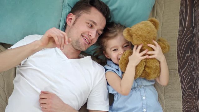 Directly above shot of cute little girl lying on floor with happy father and playing with plush toy
