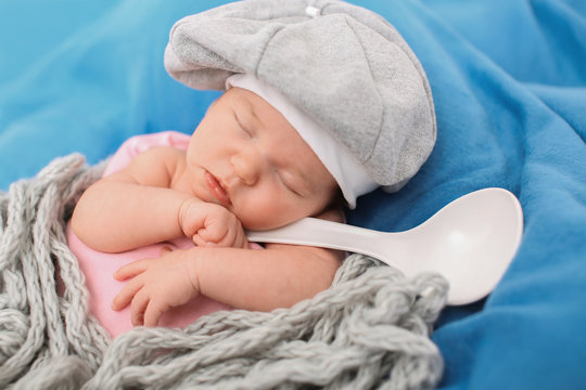 A little child in a grey cap lies witn a spoon on a blue background