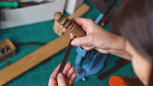 Tanner holds piece of leather and slicker in her hand. Workflow in workshop. Shooting close-up. - Powered by Adobe