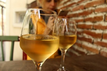 A young blond woman sitting on the terrace with two glass of white wine and looking in her cellphone