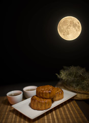 Chinese Mid Autumn Festival mooncake and tea on Wooden Bamboo Mat with Dark Background