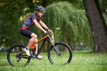 Strong guy cyclist in cycling clothes, training, improving skills, getting ready for race in park on fresh air. Man enjoying morning bike ride. Concept of motivation, healthy lifestyle