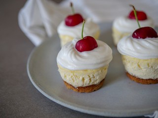 homemade personal cheesecakes with cherries and cream topping, on top of a ceramic plate