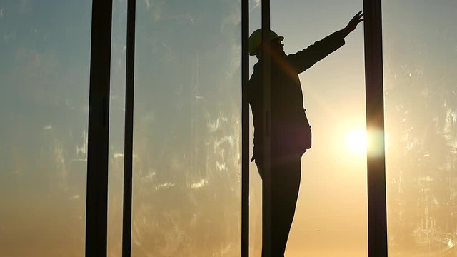 builders chief in helmet check quality of work silhouette in window frame