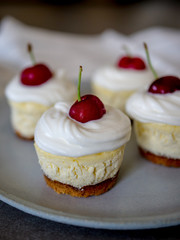 homemade personal cheesecakes with cherries and cream topping, on top of a ceramic plate