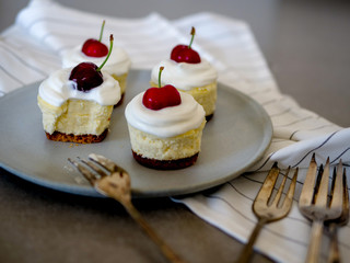 homemade personal cheesecakes with cherries and cream topping, on top of a ceramic plate