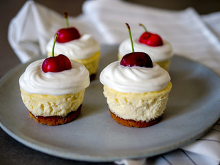 homemade personal cheesecakes with cherries and cream topping, on top of a ceramic plate