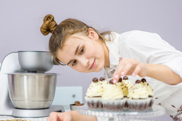 Young happy woman decorates cupcakes at kitchen