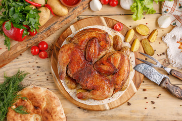 Chicken with potato garnish on a round wooden board. Still life with textiles and original cutlery. Top view.