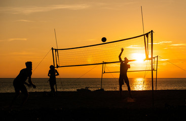 Group of silhouette tourists play volleyball on the tropical beach during the sunset time