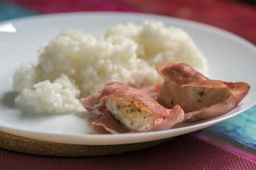 Roasted turkey meat wrapped in ham served with rice on white plate, tasty healthy lunch