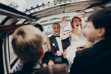 stylish happy bride and groom having fun and dancing inside of retro car smiling. emotional moment,...