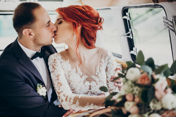 stylish happy bride and groom kissing embracing,gently hugging in retro car and smiling. emotional...