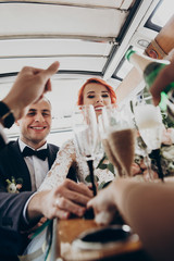 stylish happy bride and groom toasting with glasses of champagne and having fun with bridesmaids...