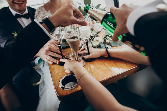 Hands With Glasses Of Champagne, Stylish Happy Bride And Groom Toasting Laughing And Having Fun With Bridesmaids And Groomsmen Inside Of Retro Car. Emotional Moment, Space For Text. Wedding Party