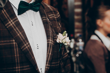 stylish boutonniere on groom brow suit. rustic bouquet and jacket close-up at wedding reception....